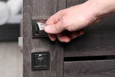 Photo of Man opening wooden door indoors, closeup of hand on handle