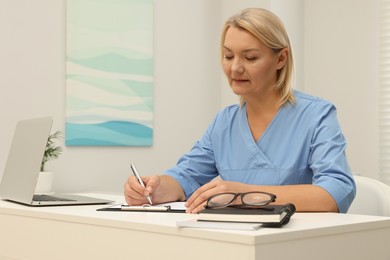 Photo of Doctor writing at white table in clinic