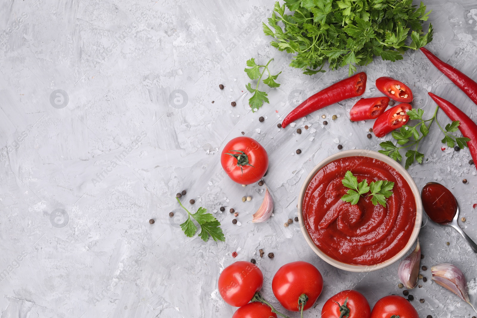 Photo of Flat lay composition with organic ketchup in bowl on grey textured table, space for text. Tomato sauce