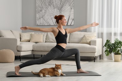 Photo of Beautiful woman with cute red cat practicing yoga on mat at home