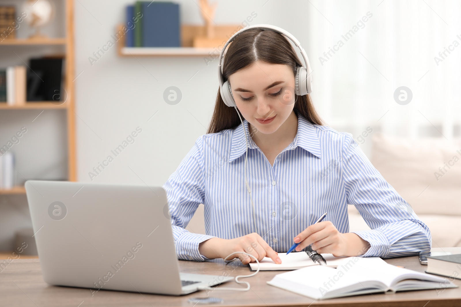 Photo of E-learning. woman taking notes during online lesson at table indoors