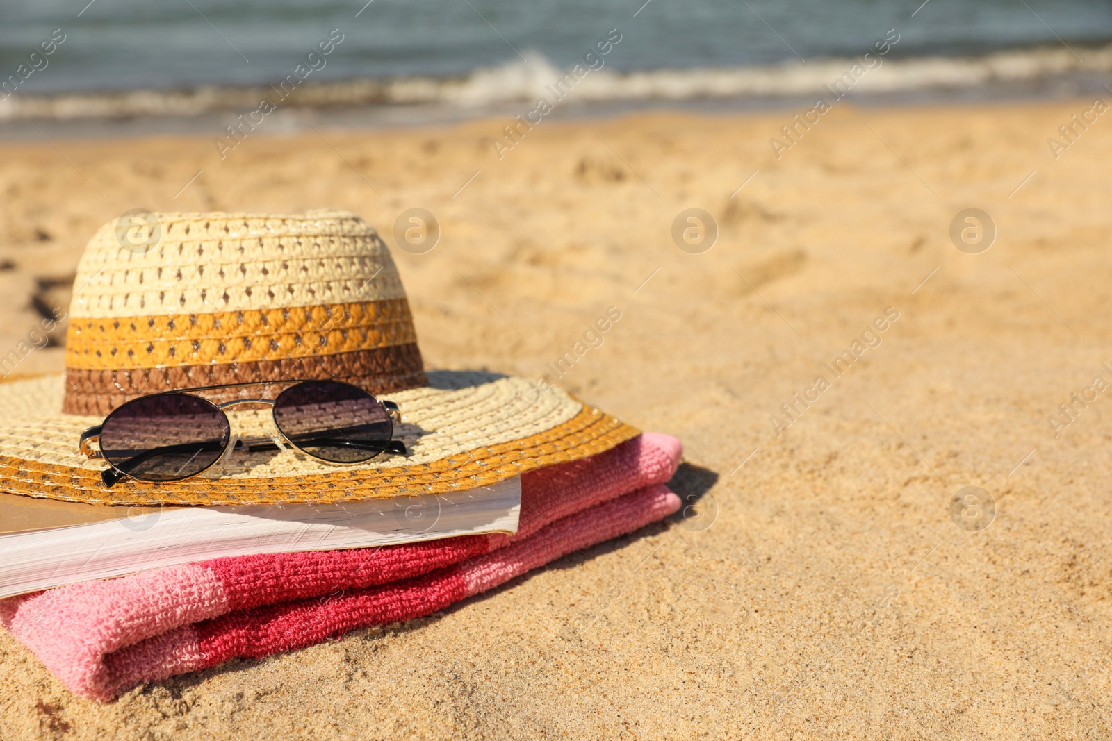 Photo of Hat, sunglasses, book and striped towel on sandy beach near sea, closeup. Space for text