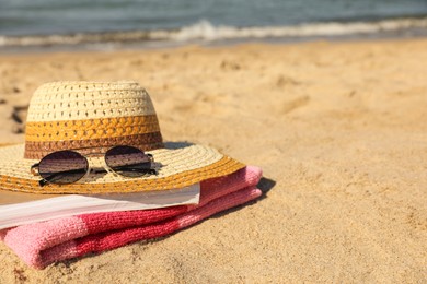 Photo of Hat, sunglasses, book and striped towel on sandy beach near sea, closeup. Space for text