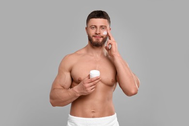 Photo of Handsome man applying cream onto his face on light grey background