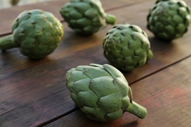 Photo of Whole fresh raw artichokes on wooden table, closeup