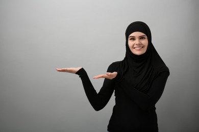 Photo of Muslim woman in hijab pointing at something on light gray background, space for text