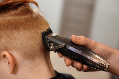 Photo of Professional hairdresser cutting boy's hair in beauty salon, closeup