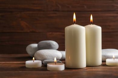 Photo of Beautiful composition with spa stones and burning candles on wooden table