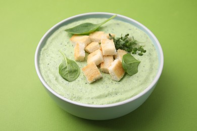 Photo of Delicious spinach cream soup with croutons in bowl on green background