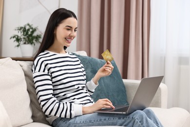 Photo of Happy young woman with credit card and laptop shopping online at home