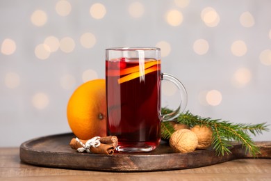 Photo of Aromatic mulled wine in glass cup on wooden table against grey background with blurred lights, closeup