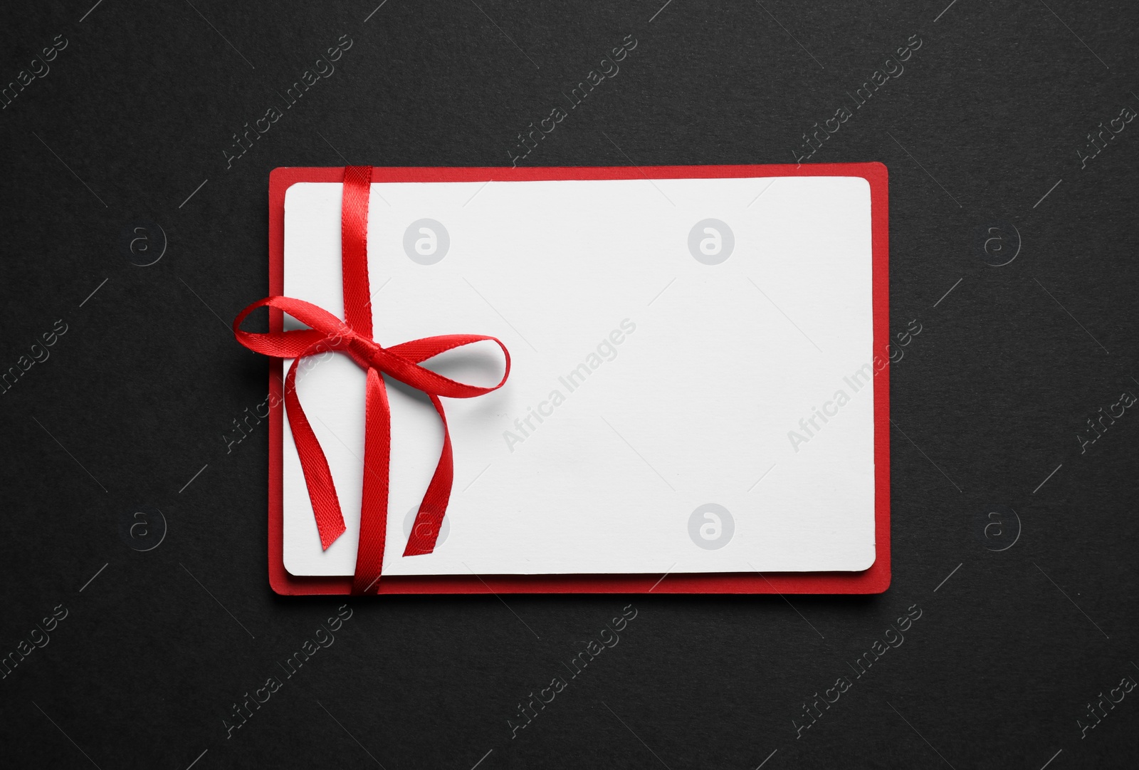 Photo of Blank gift card with red bow on black background, top view