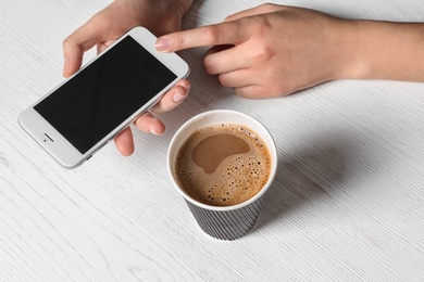 Photo of Woman using mobile phone at table with cardboard cup of aromatic coffee