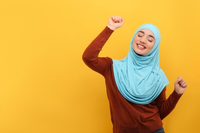 Photo of Muslim woman in hijab dancing on orange background, space for text