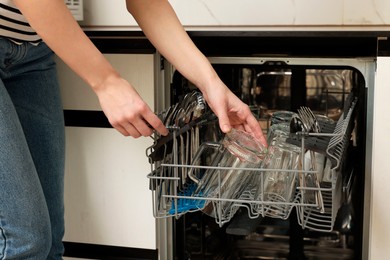 Photo of Woman loading dishwasher with glasses and plates, closeup