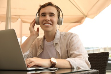 Photo of Handsome young man with headphones working on laptop in outdoor cafe