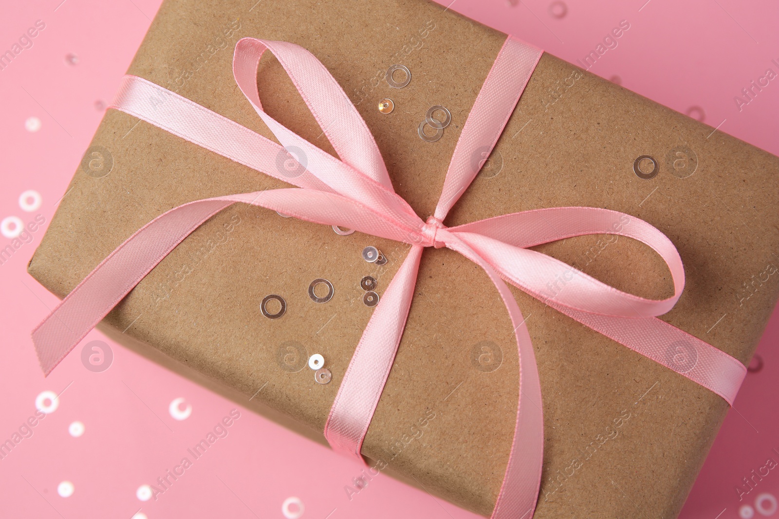 Photo of Beautiful gift box with bow and confetti on pink background, closeup