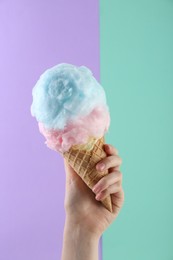 Photo of Woman holding waffle cone with cotton candy on color background, closeup