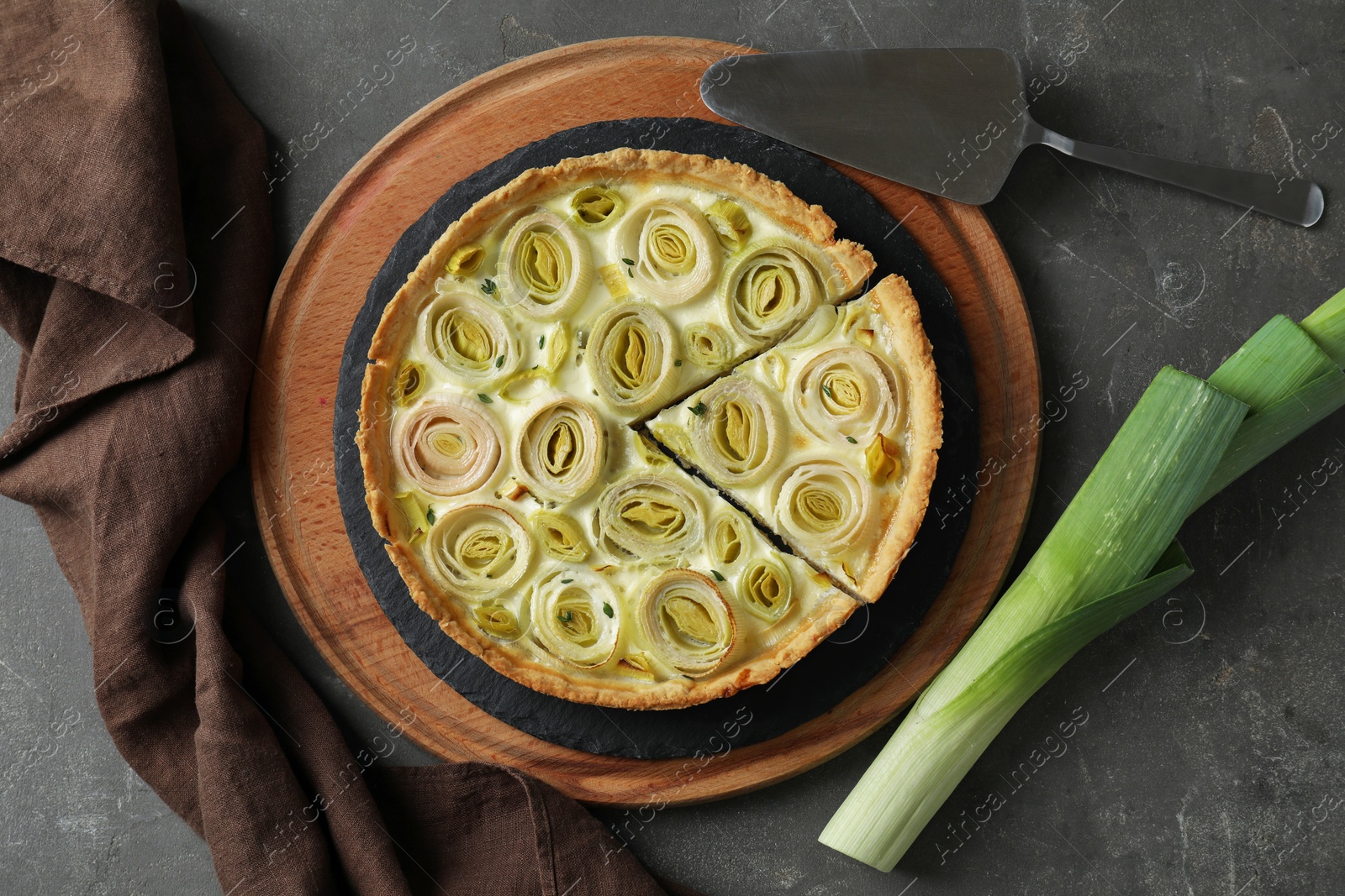 Photo of Tasty leek pie and fresh stalk on dark textured table, flat lay