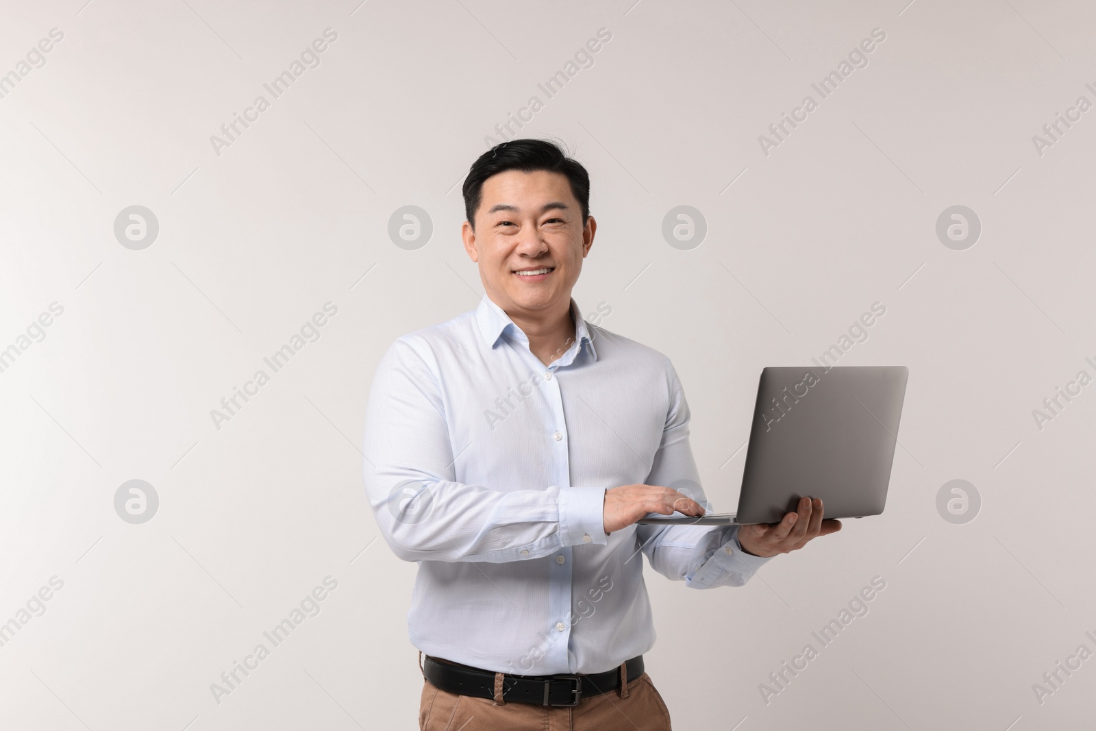 Photo of Portrait of happy man with laptop on light background