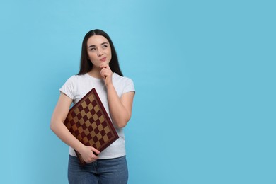 Photo of Thoughtful woman with chessboard on light blue background, space for text