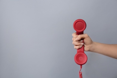 Photo of Closeup view of woman holding red corded telephone handset on light grey background, space for text. Hotline concept