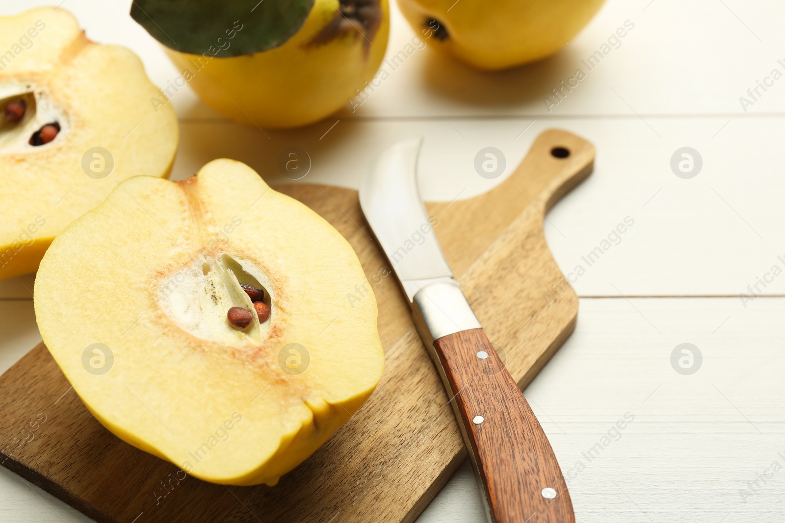 Photo of Tasty ripe quince fruits and knife on white wooden table, closeup