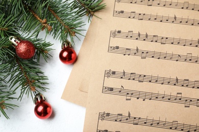 Photo of Music sheets near fir tree branches with Christmas balls on white background, flat lay