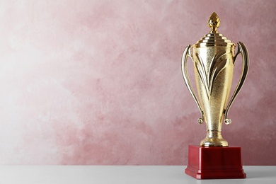 Photo of Golden trophy cup on table against pink background. Space for text