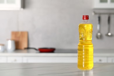 Photo of Bottle of cooking oil on white marble table in kitchen. Space for text