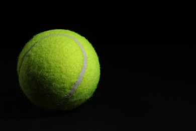 Photo of One tennis ball on black background, closeup. Space for text