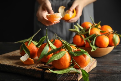 Photo of Woman peeling ripe tangerine over table on dark background, closeup