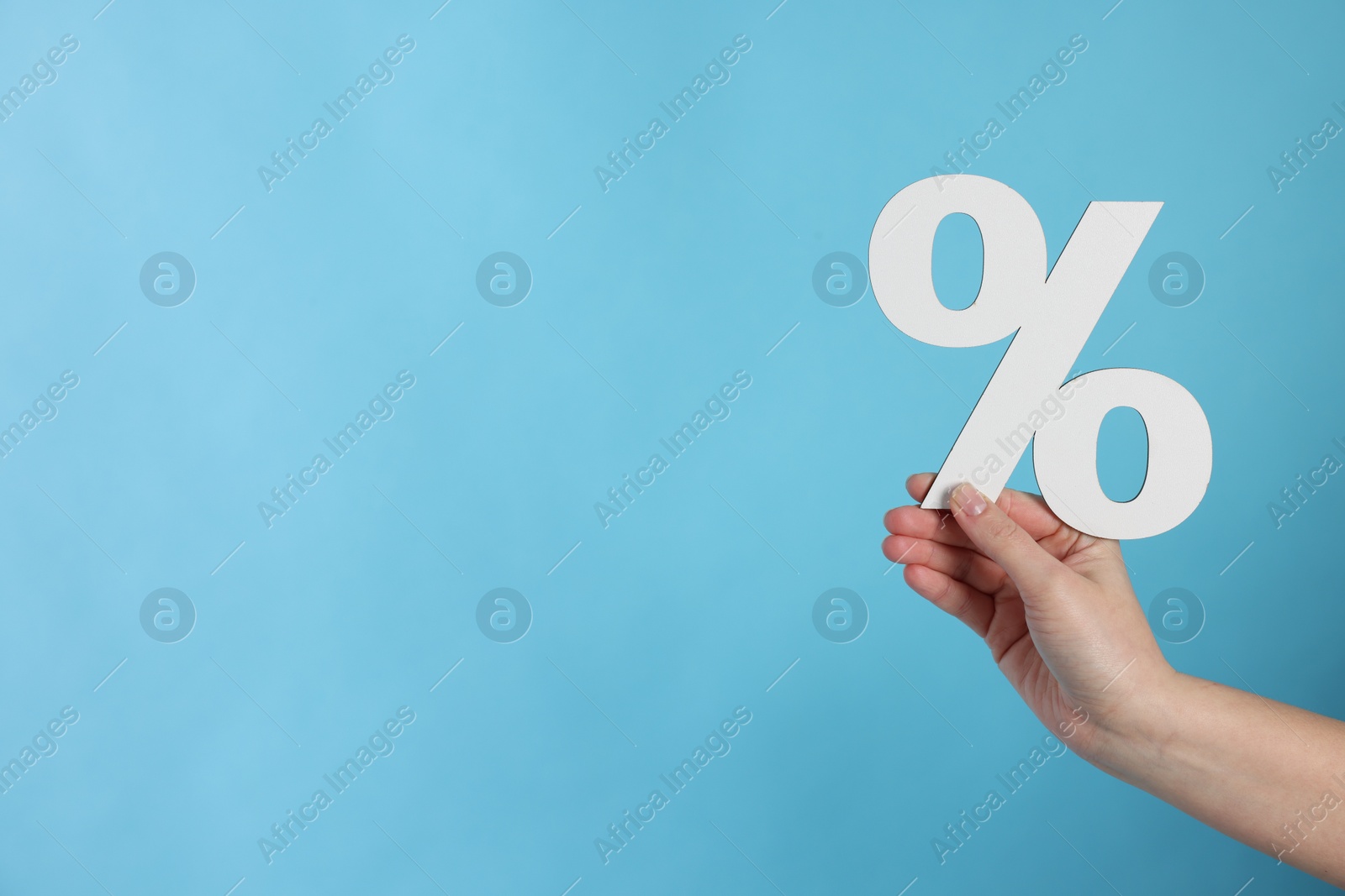 Woman holding percent sign on light blue background, closeup. Space for text Photo of Woman holding percent sign on light blue background, closeup. Space for text