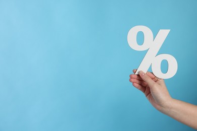 Photo of Woman holding percent sign on light blue background, closeup. Space for text
