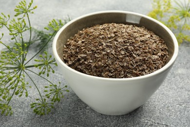 Photo of Bowl of dry seeds and fresh dill on grey table, closeup