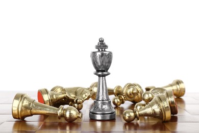 Photo of Silver king among fallen golden chess pieces on wooden board against white background
