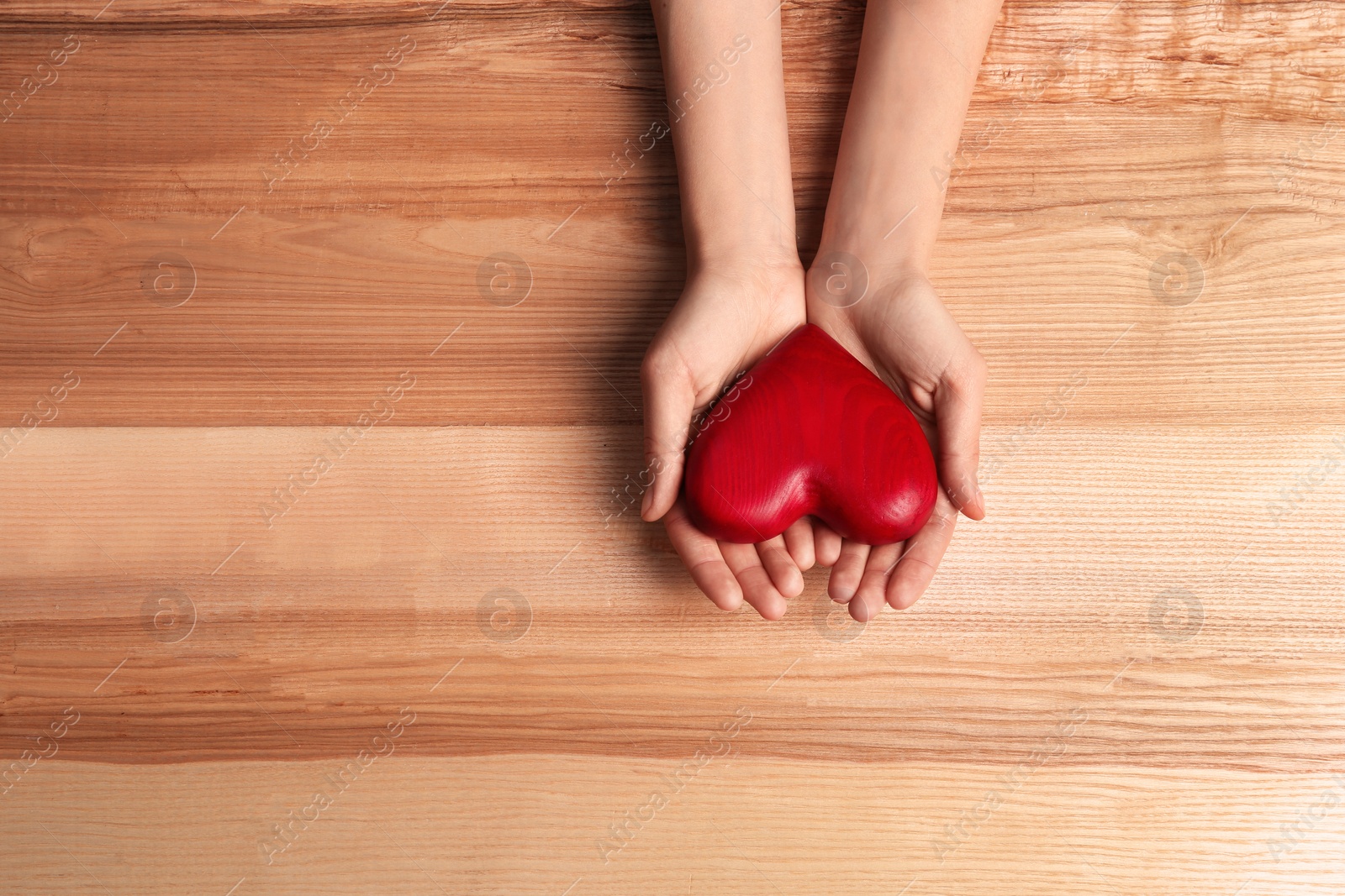 Photo of Woman holding decorative heart on wooden background, top view. Space for text