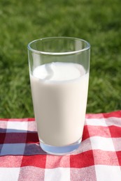 Photo of Glass of fresh milk on checkered blanket outdoors
