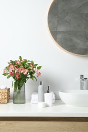 Photo of Vase with beautiful Alstroemeria flowers and toiletries near sink in bathroom