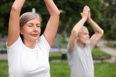 Photo of Senior couple practicing yoga in park, selective focus