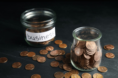 Photo of Glass jars with coins and tag BUSINESS on black table