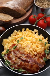 Photo of Delicious scrambled eggs with bacon in frying pan on grey table