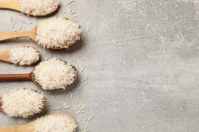 Photo of Raw basmati rice in spoons on grey table, flat lay. Space for text
