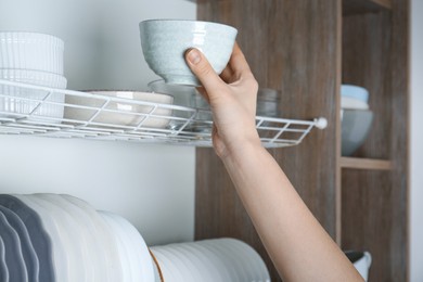 Photo of Woman taking ceramic bowl from cabinet in kitchen, closeup
