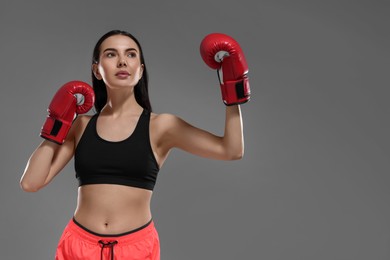 Photo of Beautiful woman in boxing gloves on grey background, low angle view. Space for text