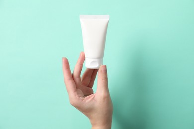 Woman with tube of hand cream on turquoise background, closeup