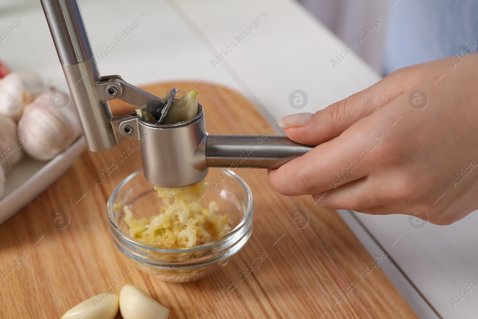 Photo of Woman squeezing garlic with press at white table, closeup