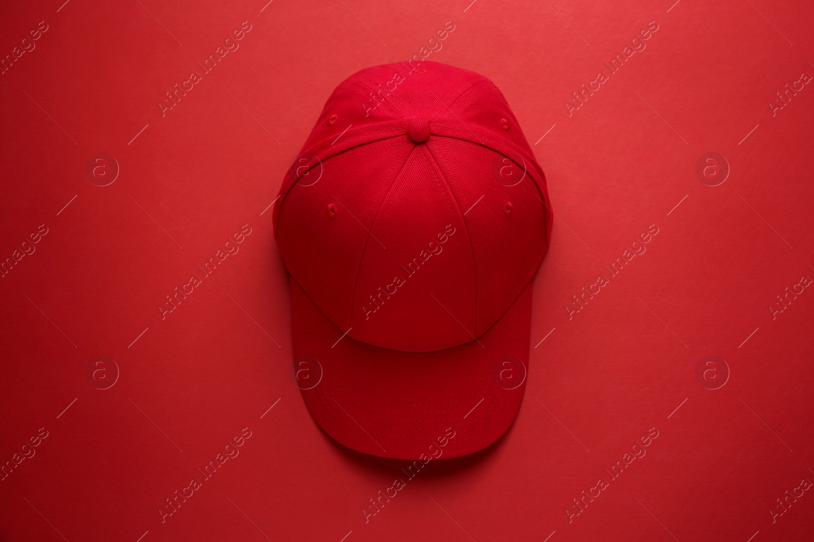 Photo of Stylish red baseball cap on color background, top view