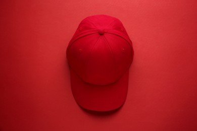 Photo of Stylish red baseball cap on color background, top view