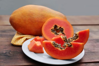 Photo of Ripe cut and whole papaya fruits on wooden table, closeup